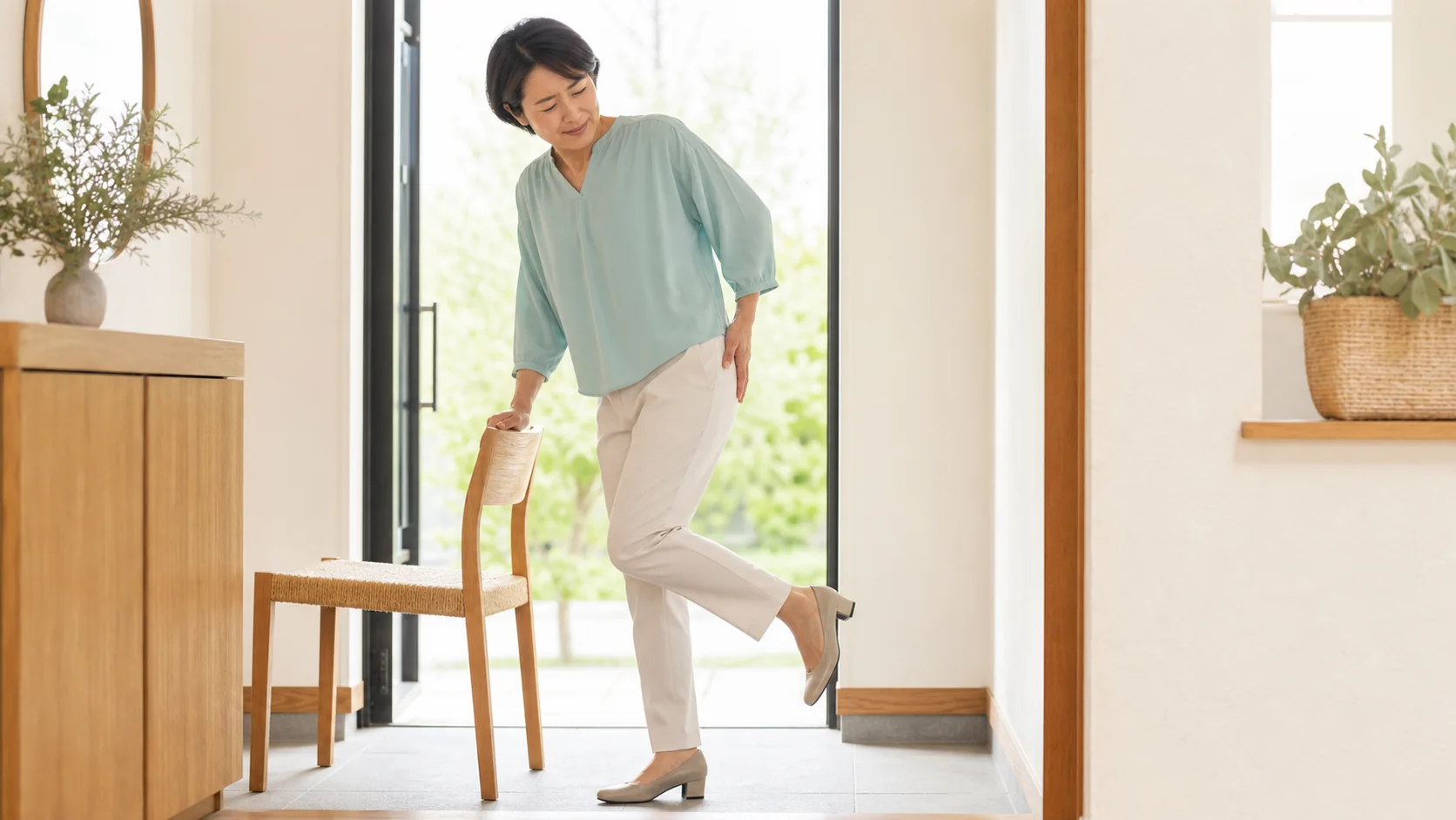 靴を履くため片脚立ちになり骨盤外側のつらさを感じている女性